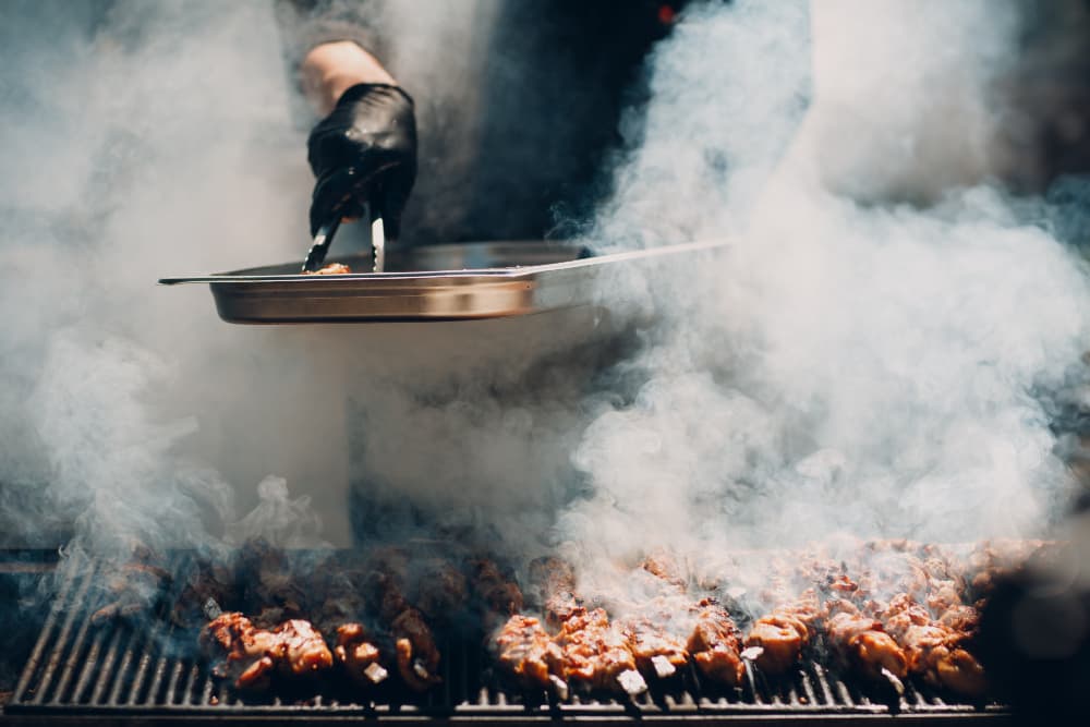 Tongs turning skewers over a smoking grill