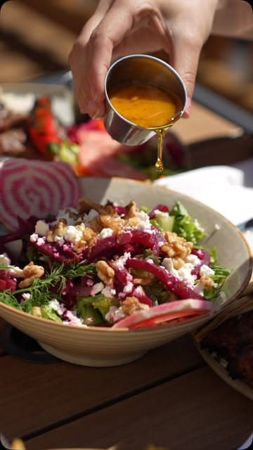 A salad with walnuts, feta and dressing being poured